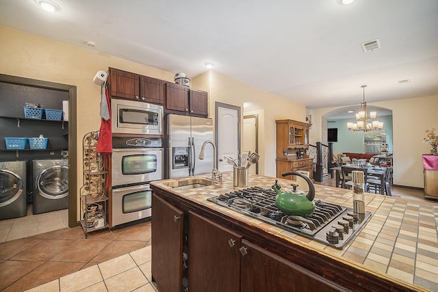 5716 Wall Ave, Haltom City, TX 76117 - kitchen with appliances with stainless steel finishes, tile countertops, washer and dryer, a chandelier, and a sink