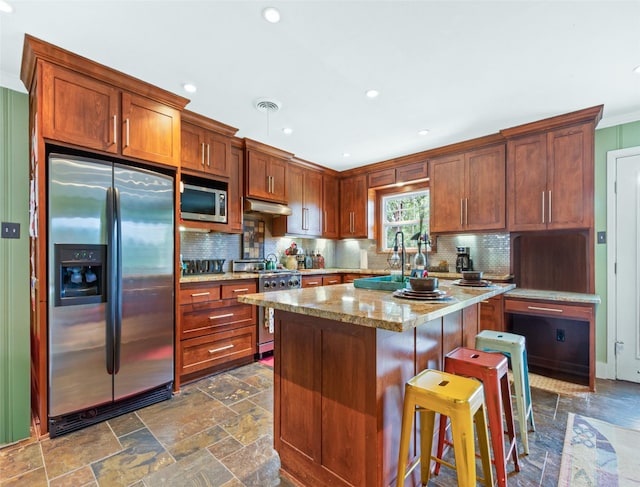 3614 Birdwell Dr, Tyler, TX 75701 - kitchen featuring stainless steel appliances, tasteful backsplash, stone tile floors, a center island, and a kitchen bar