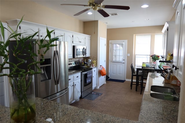 2003 Hearthside Ln, Garland, TX 75044 - kitchen with appliances with stainless steel finishes, a ceiling fan, backsplash, dark tile patterned flooring, and white cabinets