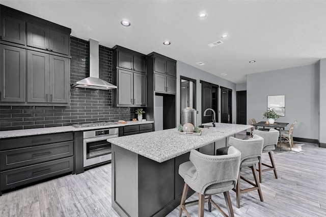 58 Lone Oak Blvd, Pottsboro, TX 75076 - kitchen with stainless steel appliances, wall chimney exhaust hood, a center island with sink, decorative backsplash, and light stone counters