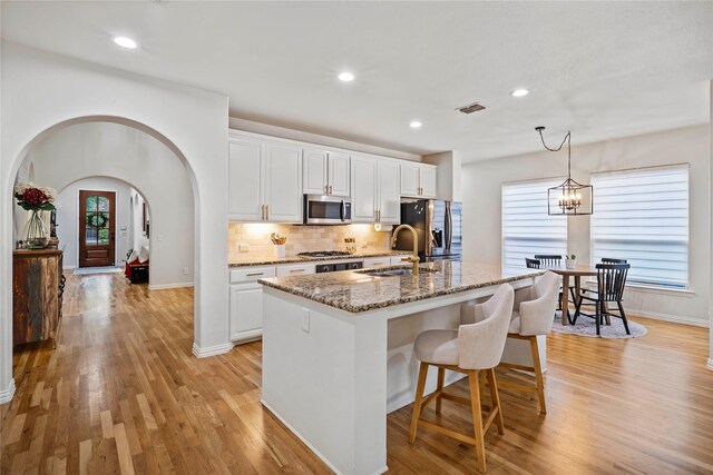 7812 Rockledge Dr, Mckinney, TX 75071 - kitchen featuring appliances with stainless steel finishes, a sink, arched walkways, a center island with sink, and light wood-type flooring