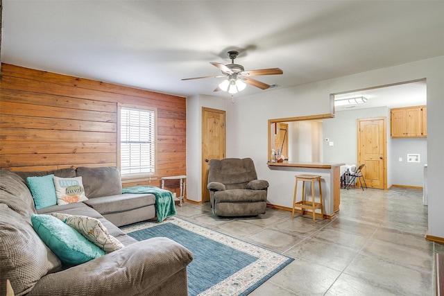 living area featuring wood walls, baseboards, and a ceiling fan