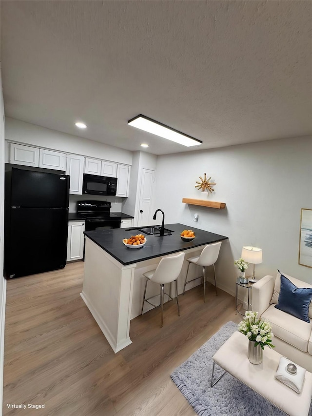 4859 Cedar Springs Rd Unit 150, Dallas, TX 75219 - kitchen featuring black appliances, dark countertops, a sink, white cabinets, and a peninsula