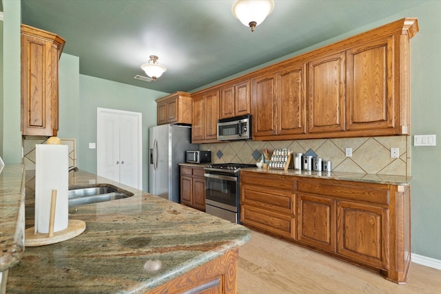 208 Burtonwood Cir, Ovilla, TX 75154 - kitchen with appliances with stainless steel finishes, a sink, backsplash, brown cabinetry, and light stone countertops