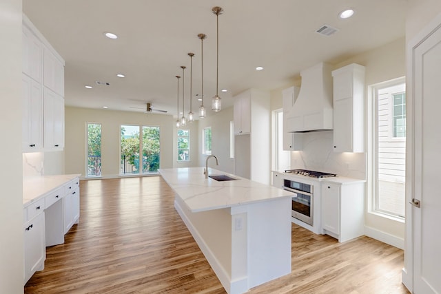 1021 Mobile St, Dallas, TX 75208 - kitchen with premium range hood, a sink, stainless steel appliances, light wood-style floors, and white cabinets
