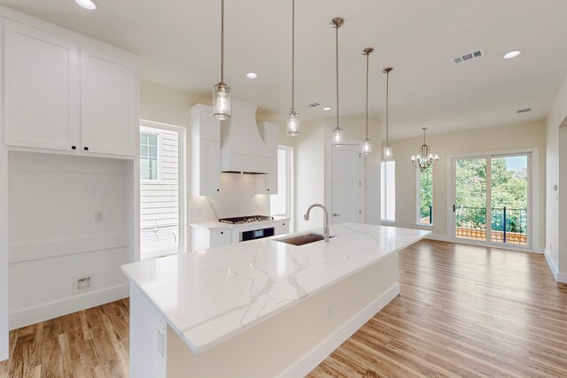 1021 Mobile St, Dallas, TX 75208 - kitchen featuring a sink, premium range hood, light wood-type flooring, white cabinets, and a chandelier