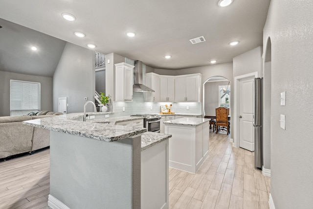 3723 Parkwood Ln, Denison, TX 75020 - kitchen featuring stainless steel appliances, wall chimney range hood, a sink, a peninsula, and arched walkways
