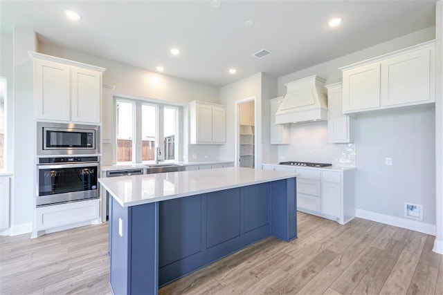 2207 Morris St, Rockwall, TX 75087 - kitchen featuring stainless steel appliances, custom exhaust hood, a center island, white cabinetry, and light wood-type flooring
