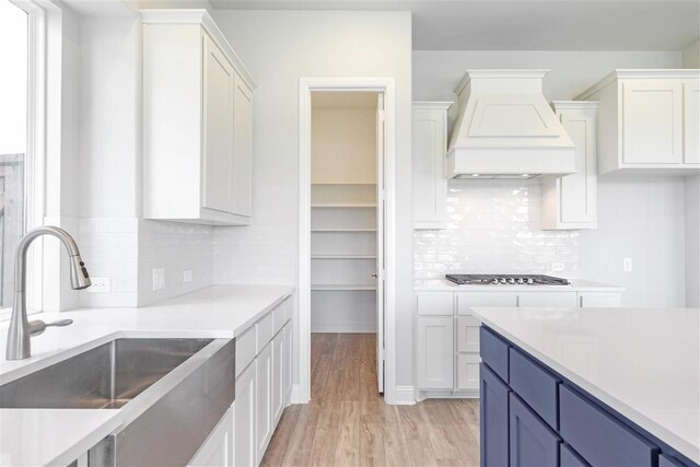 2207 Morris St, Rockwall, TX 75087 - kitchen with custom range hood, a sink, blue cabinets, stainless steel gas cooktop, and white cabinets