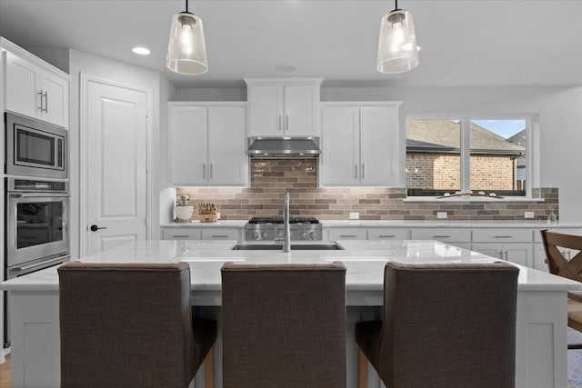 929 Lady Tessala Ave, Lewisville, TX 75056 - kitchen with appliances with stainless steel finishes, under cabinet range hood, a sink, a center island with sink, and backsplash