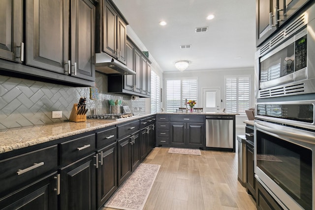 15236 Holly Bay Ct, Aledo, TX 76008 - kitchen featuring appliances with stainless steel finishes, under cabinet range hood, backsplash, crown molding, and light wood finished floors