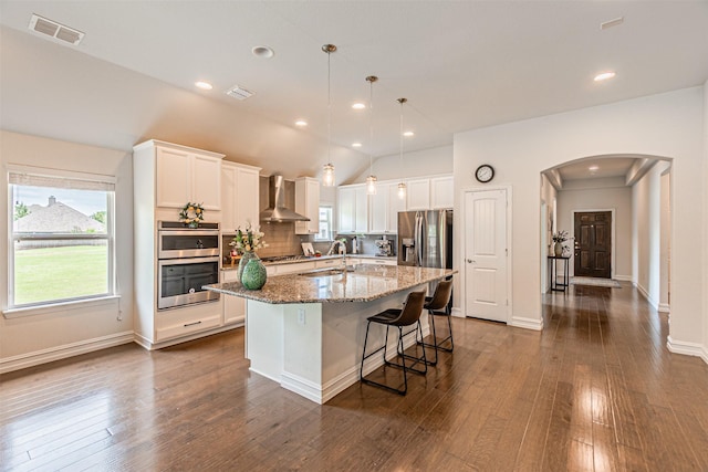 2923 Ash Ave, Melissa, TX 75454 - kitchen featuring wall chimney exhaust hood, stainless steel appliances, arched walkways, a kitchen island with sink, and white cabinetry