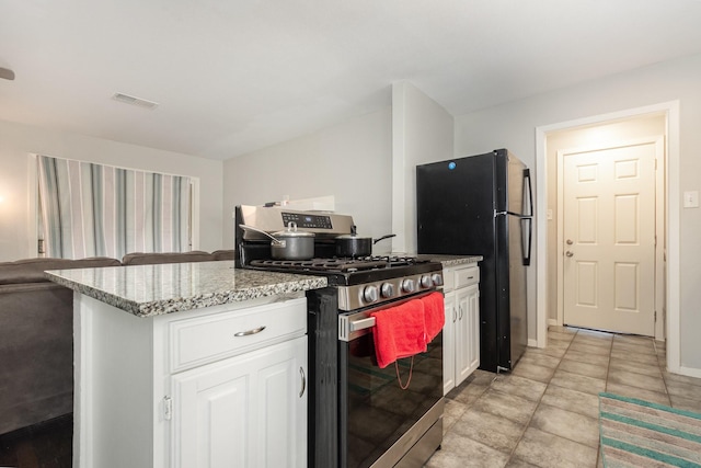2517 Blanton St, Dallas, TX 75227 - kitchen with stainless steel range with gas cooktop, freestanding refrigerator, white cabinetry, light stone counters, and open floor plan