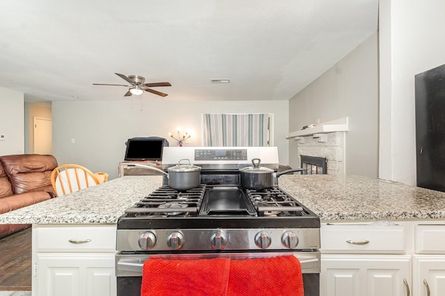 2517 Blanton St, Dallas, TX 75227 - kitchen with stainless steel gas range oven, ceiling fan, white cabinets, a stone fireplace, and open floor plan
