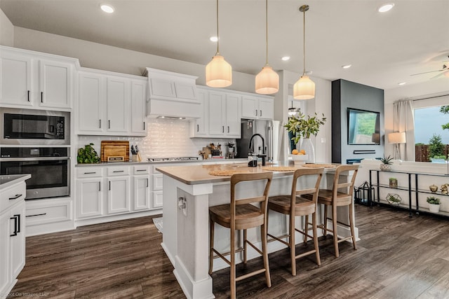 752 Fletcher Dr, Fate, TX 75087 - kitchen with appliances with stainless steel finishes, custom exhaust hood, a kitchen island with sink, decorative backsplash, and dark wood-style floors