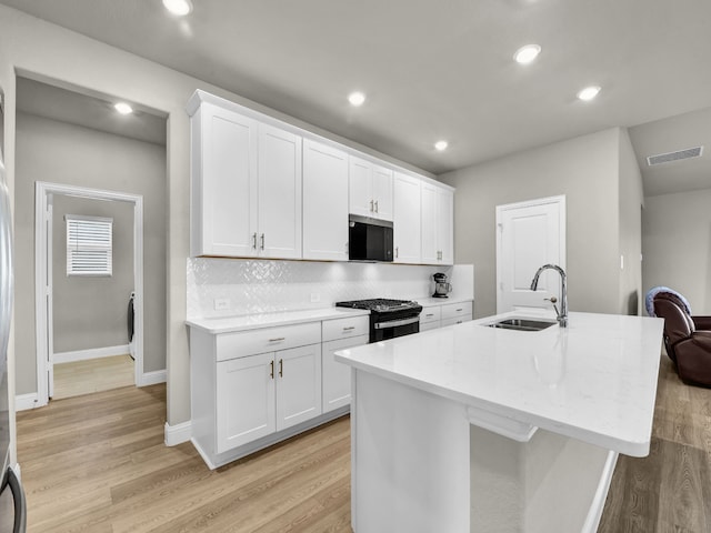 9100 Cacti Ct, Fort Worth, TX 76036 - kitchen featuring a sink, black range with gas cooktop, light wood-style flooring, white cabinetry, and an island with sink