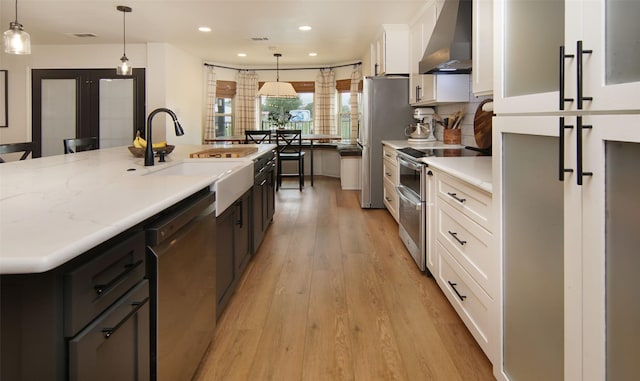 13417 Hickory Creek Dr, Haslet, TX 76052 - kitchen with wall chimney range hood, appliances with stainless steel finishes, a sink, light wood finished floors, and white cabinetry