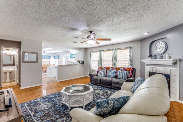 1017 Lake Trail Dr, Little Elm, TX 75068 - living area featuring ceiling fan, light wood-style floors, a tiled fireplace, baseboards, and a textured ceiling