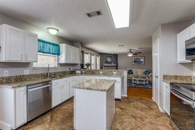 1017 Lake Trail Dr, Little Elm, TX 75068 - kitchen with stainless steel appliances, a sink, a peninsula, white cabinets, and a textured ceiling