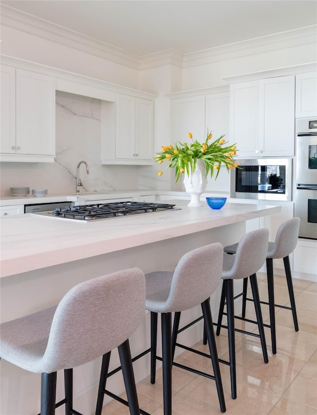 2828 Hood St Unit 1303, Dallas, TX 75219 - kitchen featuring stainless steel appliances, white cabinetry, light countertops, a breakfast bar area, and ornamental molding