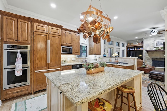 3833 Montecito Dr, Denton, TX 76205 - kitchen featuring appliances with stainless steel finishes, a kitchen island, ceiling fan, light stone countertops, and brown cabinetry