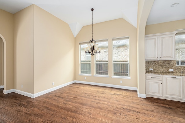 202 Woodland Pond Dr, Allen, TX 75013 - unfurnished dining area featuring arched walkways, baseboards, dark wood-style floors, a chandelier, and vaulted ceiling