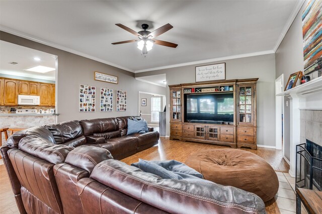 4811 Jakes Way, Midlothian, TX 76065 - living room with a ceiling fan, a tiled fireplace, crown molding, baseboards, and light wood-style floors