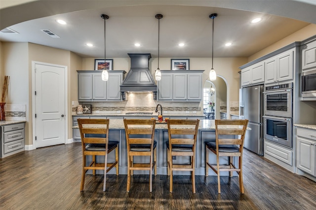 5014 Toledo Bend Dr, Frisco, TX 75033 - kitchen featuring custom exhaust hood, appliances with stainless steel finishes, arched walkways, gray cabinetry, and decorative backsplash