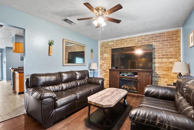 31 W Townhouse Ln Unit 20, Grand Prairie, TX 75052 - living area featuring a textured ceiling, ceiling fan, wood finished floors, a glass covered fireplace, and brick wall