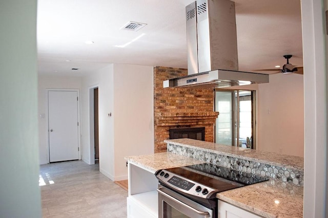 731 E Cherry St, Duncanville, TX 75116 - kitchen featuring stainless steel range with electric stovetop, island range hood, baseboards, light stone countertops, and a brick fireplace