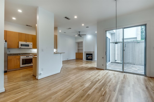 4302 Gilbert Ave, Dallas, TX 75219 - unfurnished living room with light wood-style floors, ceiling fan, a tiled fireplace, baseboards, and recessed lighting