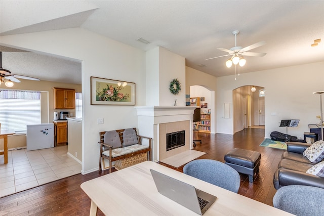 2401 Loon Lake Rd, Denton, TX 76210 - living room featuring ceiling fan, arched walkways, wood finished floors, a tiled fireplace, and vaulted ceiling
