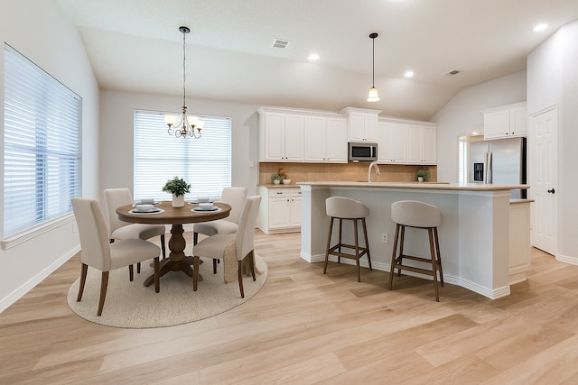 7491 Daffodil Way, Frisco, TX 75033 - kitchen with stainless steel appliances, tasteful backsplash, light wood-style floors, vaulted ceiling, and a center island with sink