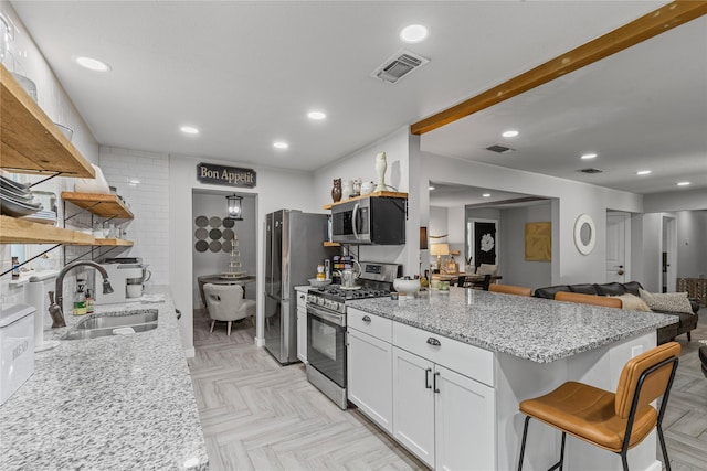 6201 Whitman Ave, Fort Worth, TX 76133 - kitchen with open shelves, stainless steel appliances, a sink, a peninsula, and white cabinetry