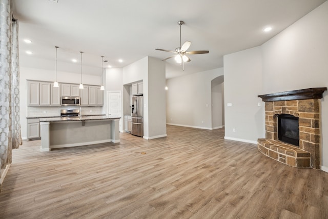 1529 Calcot Ln, Forney, TX 75126 - unfurnished living room with a ceiling fan, a stone fireplace, arched walkways, light wood finished floors, and recessed lighting