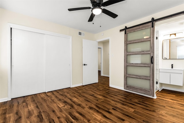 2302 Mockingbird Ln, Garland, TX 75042 - unfurnished bedroom with wood finished floors, a closet, a barn door, a ceiling fan, and baseboards