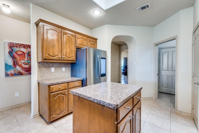 6620 Friendsway Dr, Fort Worth, TX 76137 - kitchen with smart refrigerator, a center island, arched walkways, brown cabinetry, and decorative backsplash