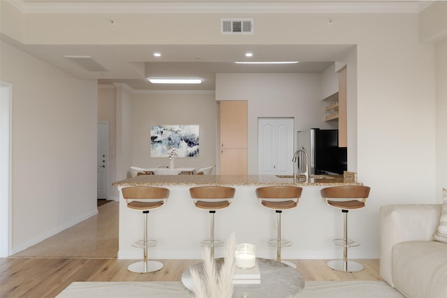 3225 Turtle Creek Blvd Unit 1012, Dallas, TX 75219 - kitchen featuring freestanding refrigerator, a breakfast bar, a sink, light wood-style flooring, and crown molding