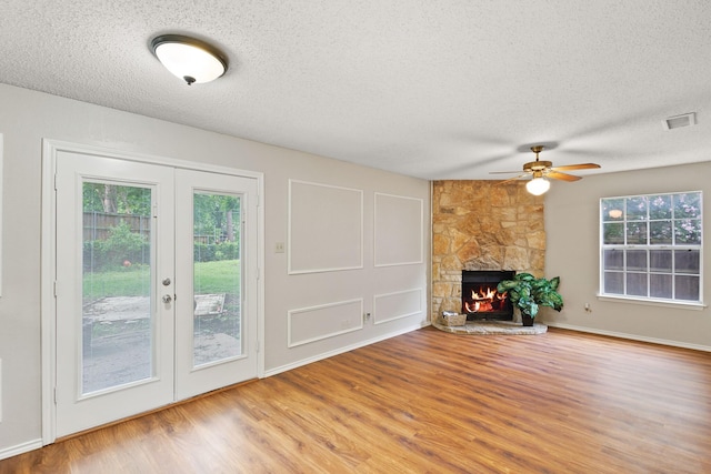 1019 W Lovers Ln W, Arlington, TX 76013 - unfurnished living room with french doors, a textured ceiling, wood finished floors, ceiling fan, and a stone fireplace