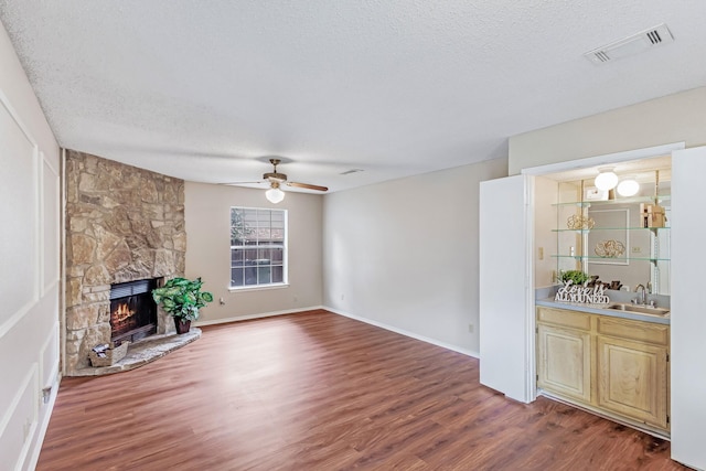 1019 W Lovers Ln W, Arlington, TX 76013 - unfurnished living room featuring wood finished floors, a textured ceiling, a fireplace, ceiling fan, and bar with sink