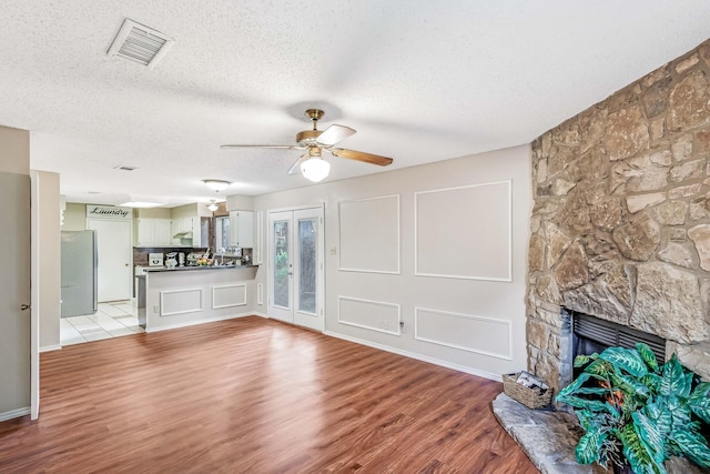1019 W Lovers Ln W, Arlington, TX 76013 - unfurnished living room with ceiling fan, a textured ceiling, light wood-style flooring, and a stone fireplace