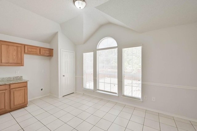 7405 Mesa Verde Trl, Fort Worth, TX 76137 - kitchen featuring vaulted ceiling, baseboards, light stone countertops, light tile patterned flooring, and brown cabinetry