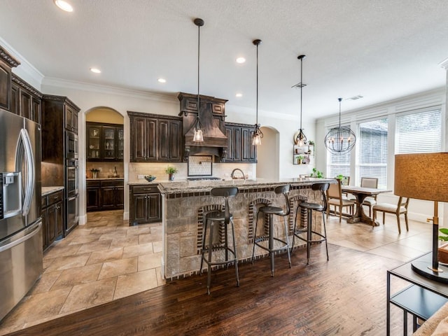 1221 Morris Dr, Keller, TX 76248 - kitchen with stainless steel appliances, arched walkways, dark brown cabinetry, an island with sink, and a kitchen bar