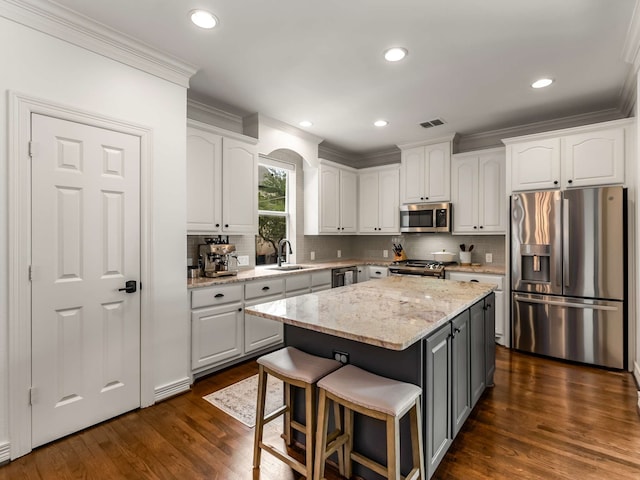 2917 Hallsville St, Dallas, TX 75204 - kitchen featuring appliances with stainless steel finishes, ornamental molding, white cabinets, a sink, and a kitchen island
