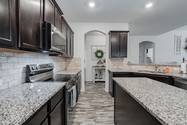 273 Pitt Cir, Fate, TX 75189 - kitchen with stainless steel appliances, a sink, arched walkways, light wood-type flooring, and light stone counters