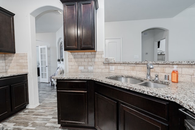 273 Pitt Cir, Fate, TX 75189 - kitchen featuring a sink, light stone counters, arched walkways, light wood finished floors, and decorative backsplash