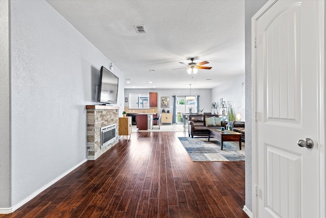 9129 Blackstone Dr, Providence Village, TX 76227 - living room featuring a ceiling fan, dark wood-type flooring, baseboards, a stone fireplace, and a textured ceiling