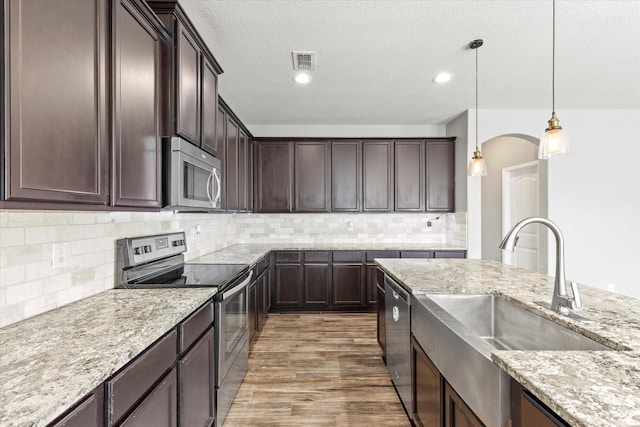 2132 Dewitt Ln, Providence Village, TX 76227 - kitchen with appliances with stainless steel finishes, a sink, dark brown cabinetry, wood finished floors, and light stone counters