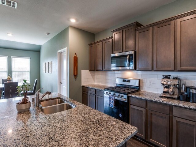 519 Stampede Ln, Princeton, TX 75407 - kitchen featuring appliances with stainless steel finishes, a sink, tasteful backsplash, light stone counters, and dark brown cabinetry