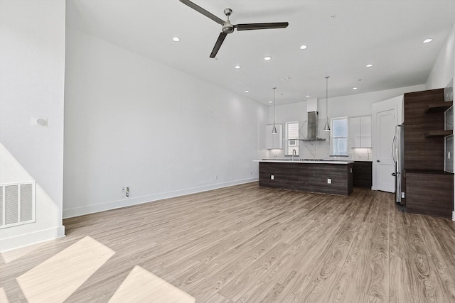 2235 Lovedale Ave Unit 102, Dallas, TX 75235 - kitchen with freestanding refrigerator, a ceiling fan, dark brown cabinetry, wall chimney range hood, and light wood-style flooring